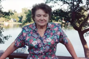 older woman in flower design blouse with lake and tree in background