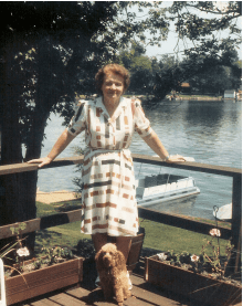 Woman in a dress with poodle at her feet and lake in background