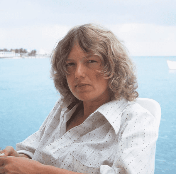 Young blond woman wearing a sceptical expression with ocean in the background.