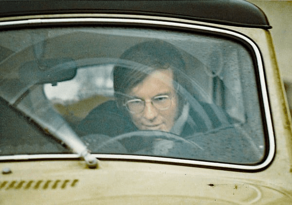 Close up of windshield of an old VW car with young man wearing glasses at the steering wheel.