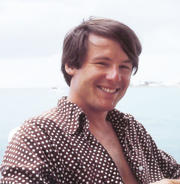 Handsome grinning young man wearing a brown and white polka dot shirt by the ocean.