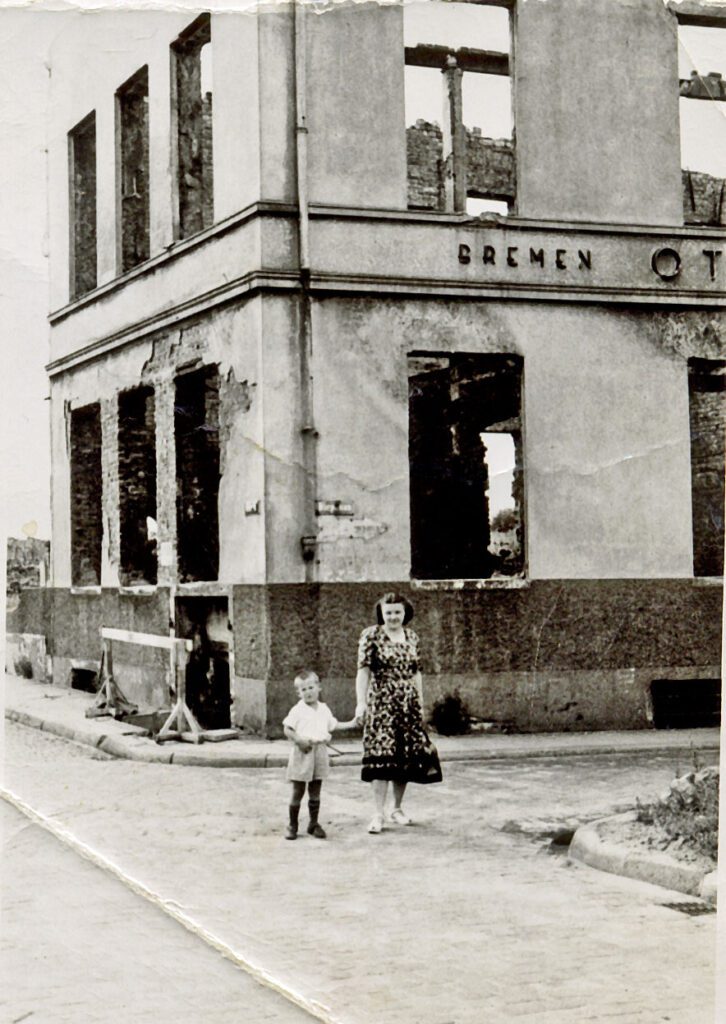 Old photo of young woman holding the hand of her small son in front of a bombed out building in Bremen in 1948.