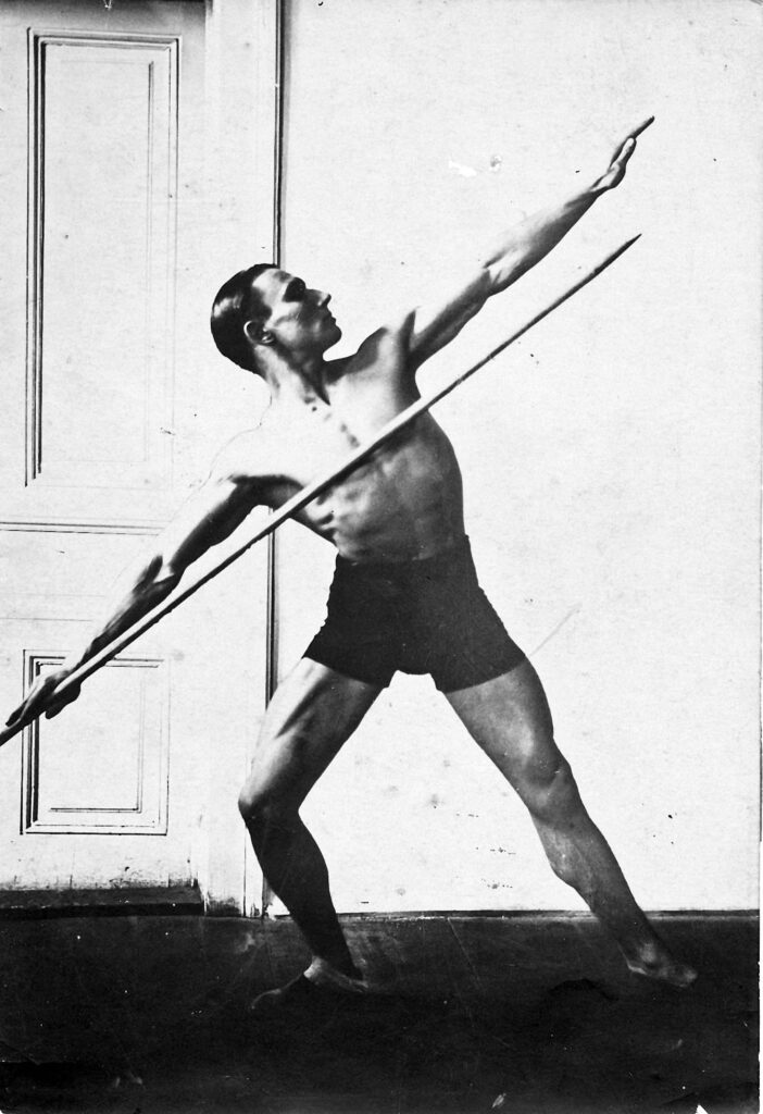 Black and white photo of physically fit handsome male gymnast posing with javelin.