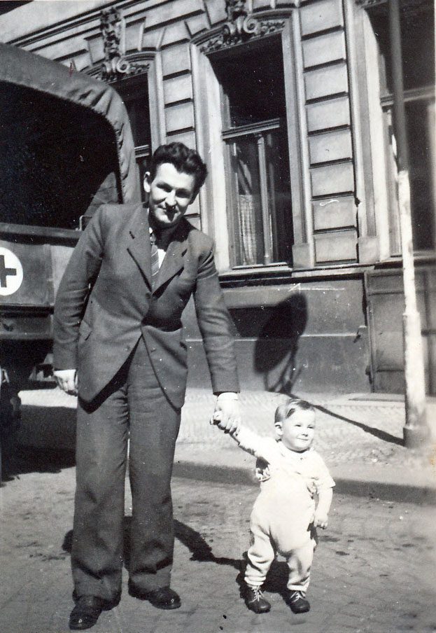 Smiling man in rumpled suit holding hand of small toddler boy.