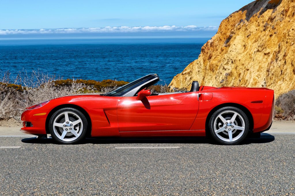 shiny red corvette sports car parked on steep cliff near the ocean.