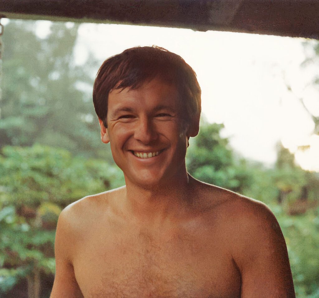 Grinning handsome young man without a shirt with forest in the background.