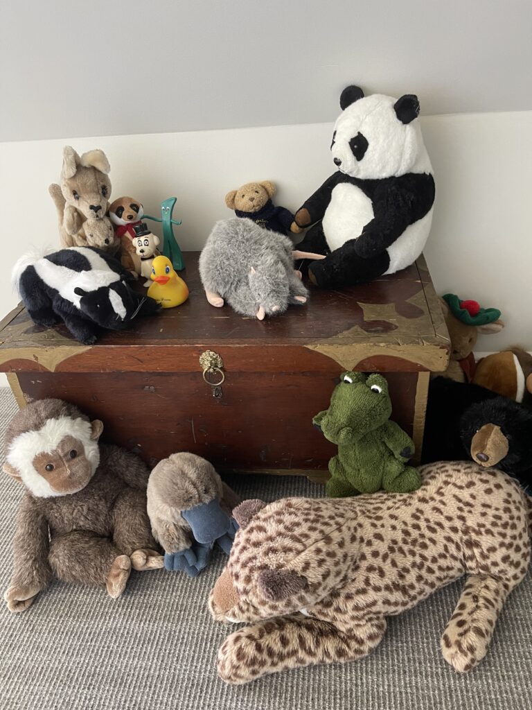 An old wood toy chest with barious stuffed animals around it.